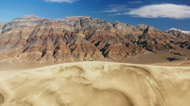 People hiking to the top of high sand dune with painted mountains landscape on motion background. Tourists walking by golden dune hills under blue sky. Nature 4K. Travelers exploring wilderness desert