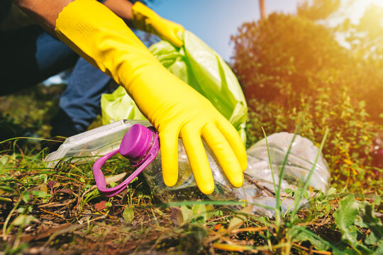 Volunteer in yellow gloves collecting garbage in trash bag outdoors on a sunny summer day. Picking up garbage in nature. Concept of environmental protection. People and ecology.