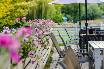 Outdoor cafe interior with wooden furniture, rotan chairs and purple flowers for decoration. Selective focus.