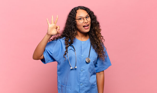 young hispanic woman feeling happy, relaxed and satisfied, showing approval with okay gesture, smiling. nurse concept