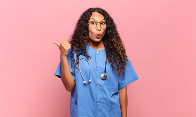 young hispanic woman looking astonished in disbelief, pointing at object on the side and saying...