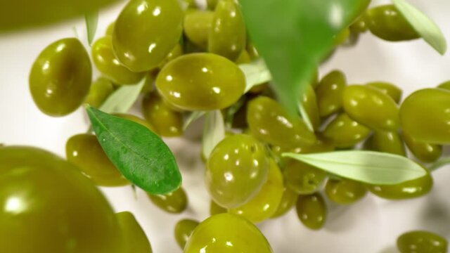Super Slow Motion Shot of Falling Fresh Green Olives and Leaves on White Background at 1000 fps.