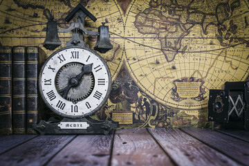 still life composed of antique books, camera and clock on a background of a classic map.