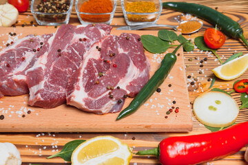 Raw pork meat on wooden cutting board at kitchen table for cooking pork steak roasted or grilled with ingredients herb and spices , Fresh pork