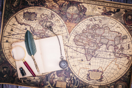 zenithal view of still life composed of old books, pistols, pen with ink, camera and clock on a background of a classic map.
