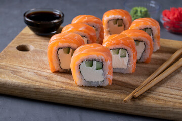 Sushi set with salmon and with philadelphia cheese on wooden board on gray background. Healthy food.