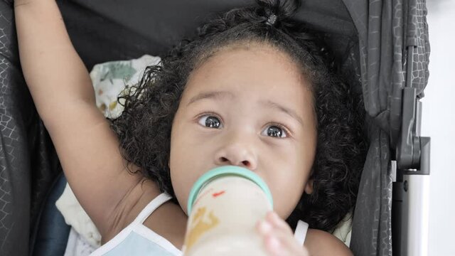 Close up Slow motion of Mixed race black girl Ethnicity Thai-Nigeria 3 year old child is drinking milk from a bottle on the stroller