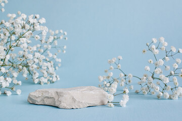 A minimalistic scene of a lying stone with flowers on a light blue background. Catwalk for the...