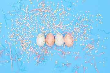 Minimal easter concept. Flat lay composition of four eggs with colorful foam balls, confetti on blue backdrop, copy paste for text, top view. Modern design template of postcard, banner, greeting card