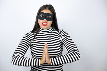 Young beautiful brunette burglar woman wearing mask begging and praying with hands together with hope expression on face very emotional and worried