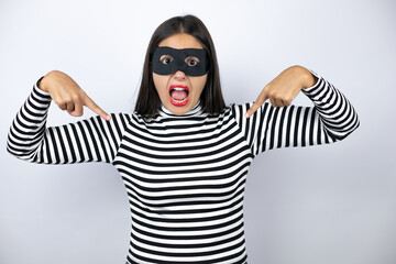 Young beautiful brunette burglar woman wearing mask looking confident with smile on face, pointing...