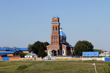 An active Orthodox high red brick church on a summer day in a small village in the European part of Russia.
