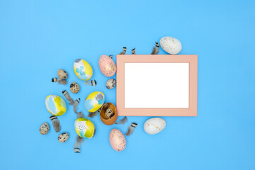 Flat lay image composition of Easter eggs, feathers on blue background, pink coral frame with space for text, top view. Minimal easter concept. Modern design template of postcard. View from above