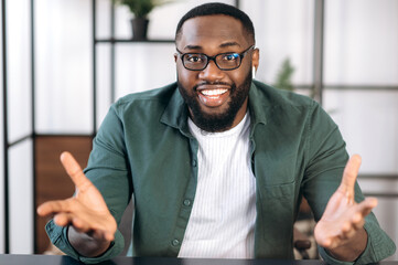 Successful friendly multiracial black male freelancer, business leader or tutor, speaking during video conference with colleagues or friends, gesturing hands and smiling, talks about plans,strategy