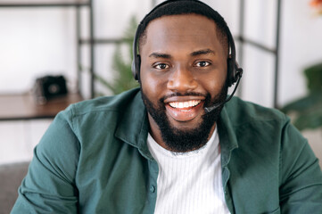 Close-up portrait of an attractive confident bearded African American operator of call center or business leader. Black businessman in headset and casual shirt looks at the camera and friendly smiling