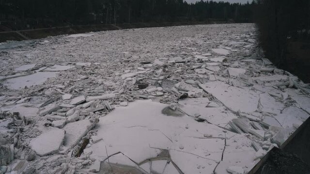 Huge Ice Loads Drift in the River Ogre, Latvia. Stedicam Shot in Snowy Mart Day. Congestion on the River in the Spring. A Large Cluster of Moving Ice Blocks