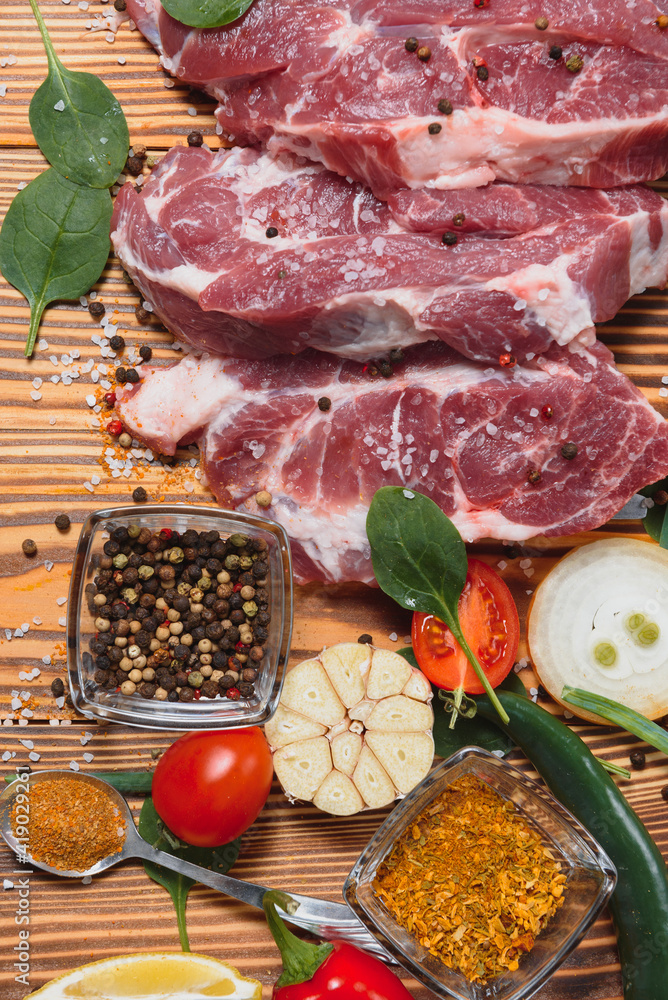 Wall mural Raw pork meat on wooden cutting board at kitchen table for cooking pork steak roasted or grilled with ingredients herb and spices , Fresh pork