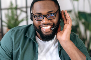 Webcam view of a handsome confident bearded African American employee, operator of call center. Black businessman in a headset and eyeglasses looks at the camera and friendly smiling