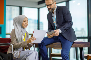 Female muslim officer is sitting on the wheelchair while she present her idea on the document to...