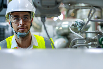 Men industrial engineer wearing a white helmet while standing in a heavy industrial factory behind. The Maintenance looking of working at industrial machinery and check security system setup in fact