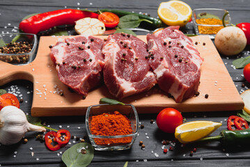Raw pork meat on wooden cutting board at kitchen table for cooking pork steak roasted or grilled with ingredients herb and spices , Fresh pork
