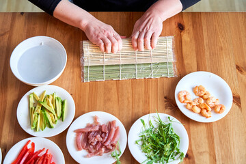 young woman prepares sushi with fresh ingredients at home. on wooden table.