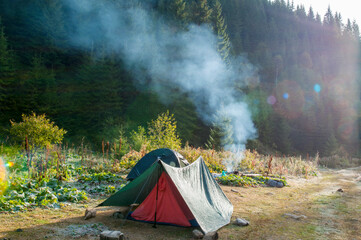 tourist tent stands on a green meadow against the backdrop of forests and peaks