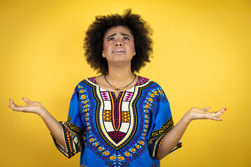 African american woman wearing african clothing over yellow background clueless and confused expression with arms and hands raised