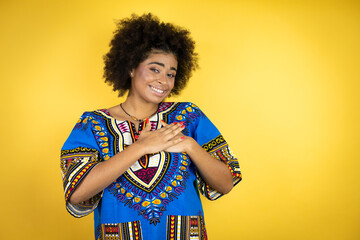 African american woman wearing african clothing over yellow background smiling with her hands on her chest and grateful gesture on her face.