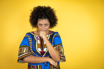 African american woman wearing african clothing over yellow background with her hand to her mouth because she's coughing