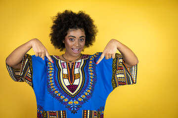 African american woman wearing african clothing over yellow background looking confident with smile on face, pointing oneself with fingers proud and happy.