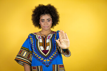 African american woman wearing african clothing over yellow background serious and doing stop sing with palm of the hand.