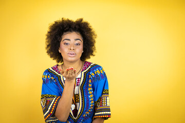 African american woman wearing african clothing over yellow background looking at the camera blowing a kiss with hand on air being lovely and sexy. Love expression.