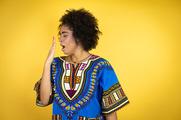 African american woman wearing african clothing over yellow background bored yawning tired covering mouth with hand. Restless and sleepiness.