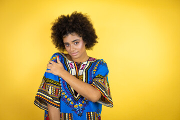 African american woman wearing african clothing over yellow background with pain on her shoulder and a painful expression