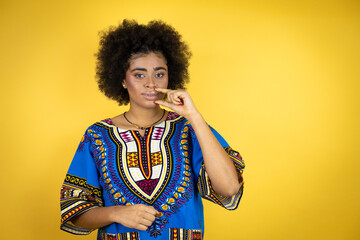 African american woman wearing african clothing over yellow background mouth and lips shut as zip...