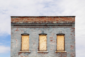 Top of an Old Brick Building with Three Boarded Windows against a Cloudy Sky