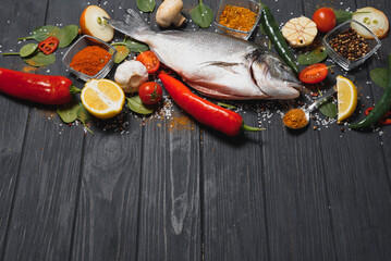 Raw sea fish dorado with lemon, pepper, tomatoes and various spices. On a black rustic background.