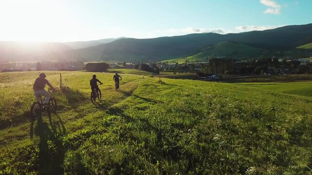 Following aerial shot of mountain bikers riding downhill into a beautiful valley. Group of friends cycling on a beautiful sunny day