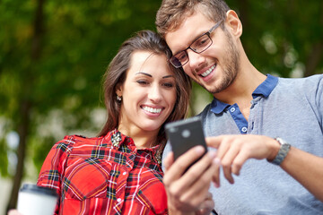 Happy couple with smart phone. Happy young loving couple standing outdoors together and looking at the mobile phone together
