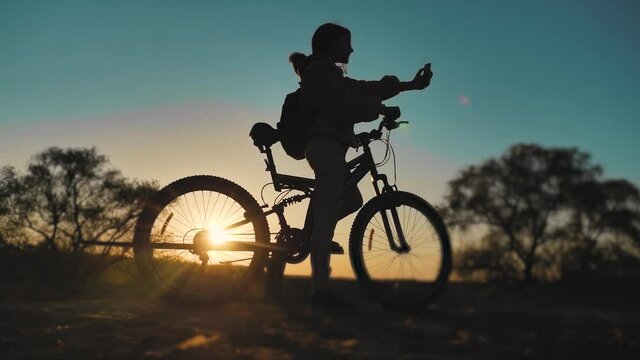 teenage girl photographs herself on a smartphone with a bicycle rides in the park at sunset on nature. healthy girls lifestyle and bike makes selfie