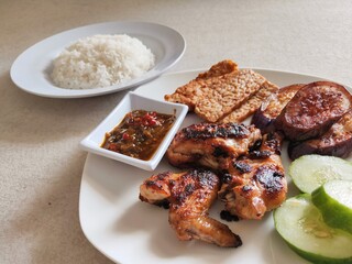Ayam Bakar, Sambal, Tempeh, Eggplant and Cucumber on White Plate.
