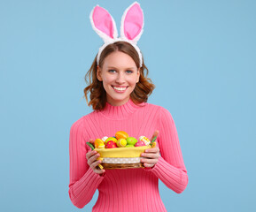 Positive young woman with bunny ears smiling and holding Easter basket in hands