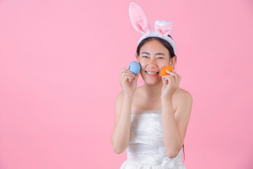 Obraz na płótnie Canvas smiling happy young woman wearing bunny ears and holding a of Easter eggs on pink background
