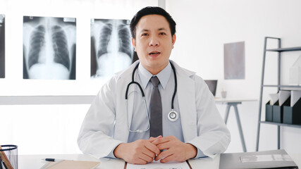 Young Asia male doctor in white medical uniform with stethoscope using computer laptop talk video conference call with patient, looking at camera in health hospital. Consulting and therapy concept.