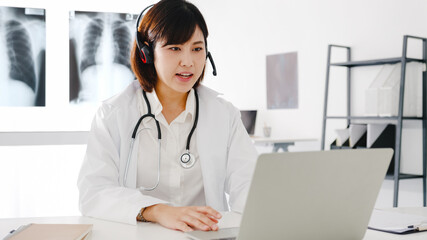 Young Asia female doctor in white medical uniform with stethoscope using computer laptop talking...