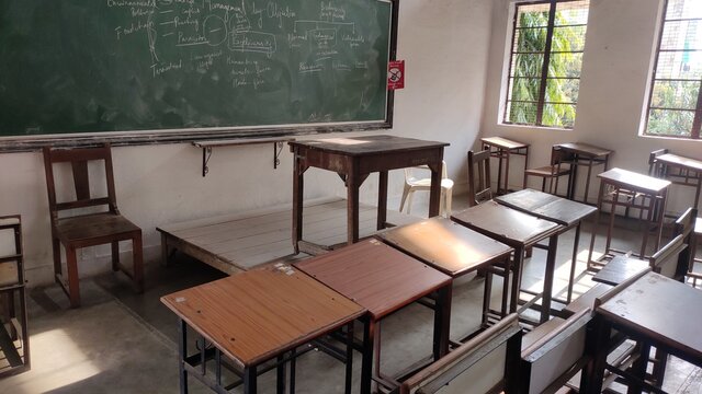 Classroom with a green color study board with wooden study tables and teachers desk with light coming from window 