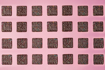 Chocolate biscuit topping with square shape isolated on pink background. The chocolate biscuit pattern is neatly arranged. Chocolate biscuit wallpaper. Biscuit mock up. Delicious yet delicious snacks.