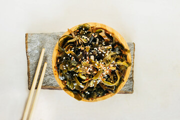 seaweed salad with sesame seeds on round bamboo plate on stand made of natural gray stone . trending image of traditional Asian cuisine, top view, selective focus