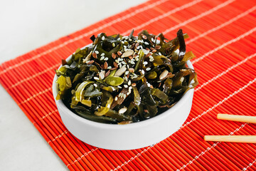 asian salad of canned sea kelp, with onion and sesame seeds in a white round plate on a red Asian napkin and chopsticks. selective focus